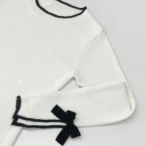 Nahaufnahme eines eleganten weißen Pullovers mit Kontrastbesatz und Samtschleife am Ärmel.