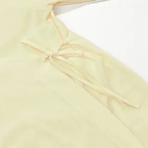 Nahaufnahme des seitlichen Bindebands am hellgelben Kleid mit feiner Stofftextur.