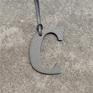 Grey leather letter C bag charm detail shot, stylish handbag pendant accessory with strap.