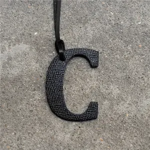 Close-up view of black leather letter C bag charm pendant accessory showcasing fine texture.