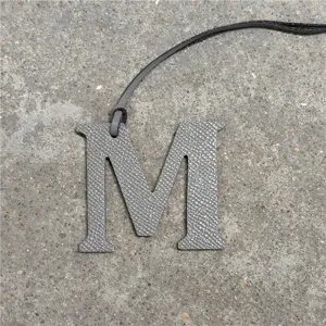 Grey leather letter M bag charm pendant, stylish alphabet keyring accessory for purses and cars.