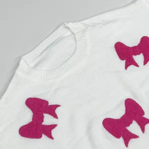 Nahaufnahme eines weißen Pullovers mit weichen rosa Schleifenapplikationen und Rundhalsausschnitt.