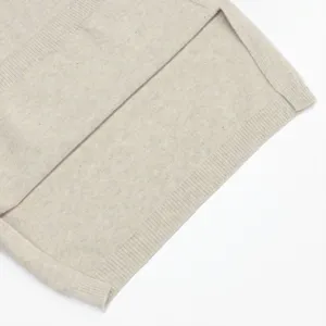 Vista detallada de un elegante chaleco de punto beige con abertura lateral y dobladillo.