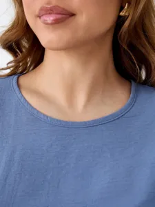 Close-up detail of women's blue crew neck top and stylish gold earring accessory.