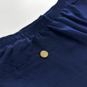 Détail de pantalon lounge bleu foncé, avec ceinture élastique et bouton doré texturé.