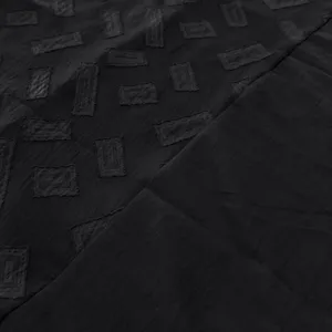 Gros plan sur le tissu de l'ensemble noir montrant un motif texturé géométrique élégant.