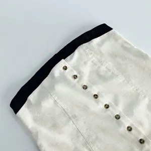 Linen dress detail featuring contrast black waistband and tortoiseshell buttons close-up.