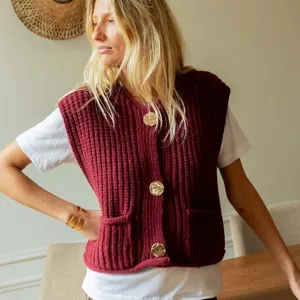 Detailed view of the sleeveless burgundy knit vest featuring large gold buttons and front pockets.