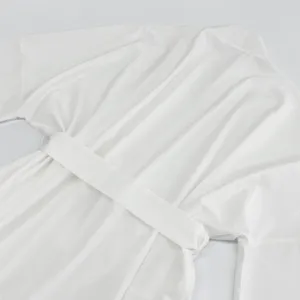 Dettaglio di lunga vestaglia bianca unita con cintura, tessuto morbido ed elegante cardigan.