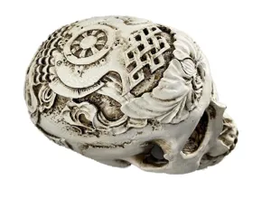 Detailed resin skull carving ornament with traditional relief patterns, close-up view.