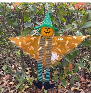 Halloween hanging decoration featuring a pumpkin head, witch hat, and bat wings in outdoor setting.