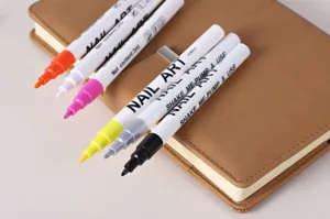 Gedetailleerde close-up van kleurrijke nail art pennen op bruin leren notebook.
