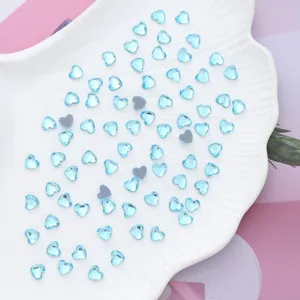 Close up of light blue heart-shaped crystal rhinestones scattered on a white shell dish for nail art