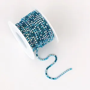 Primer plano de una cadena de estrases azules en bobina blanca, ideal para manualidades.