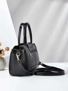 Detail van zwart lakleren handtas, krokodillenstructuur, elegante metalen hardware en riem.