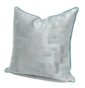 Detailed view of silver-grey throw pillow with blue piping and abstract geometric pattern.