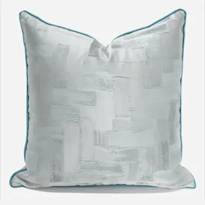 Modern decorative throw pillow with silver grey geometric pattern and blue piping for sofa chair.