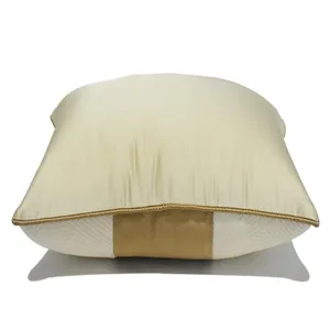 Vue détaillée du coussin décoratif beige de luxe avec une bande et un passepoil dorés.