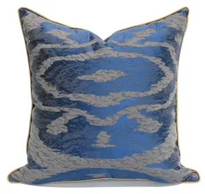 Gros plan détaillé de la housse de coussin géométrique bleu et gris avec passepoil doré.