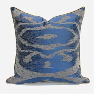 Housse de coussin décorative bleue et grise avec un motif abstrait et liseré doré.
