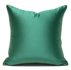 Close-up view of a luxury green satin pillow cover featuring elegant gold piping detail.