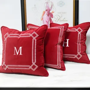 Housse de coussin en velours rouge avec bordure géométrique brodée blanche et lettre.