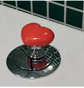 Heart-shaped toilet flush button accessory, red heart toilet tank push button detail view.