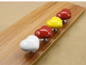 Close-up detail of colorful heart-shaped ceramic cabinet knobs mounted on a wooden sample board.