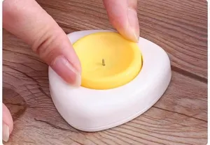 Close-up view of a yellow and white egg pricker showing manual pressing operation detail.