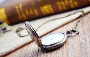 Close-up view of a vintage pocket watch with a delicate chain on a rustic wooden background.
