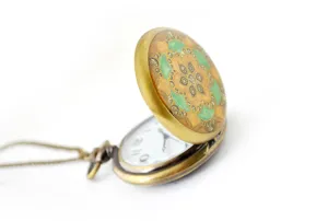 Close-up detail of vintage bronze pocket watch with colorful resin floral pattern and chain.