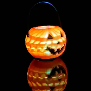 Close-up of a glowing Halloween pumpkin candy bucket with black handle on dark reflective surface.
