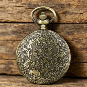 Detailed view of vintage bronze pocket watch with intricate floral engraved pattern on wood background.