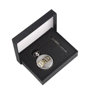 Detail de montre de poche argent texture avec texte DAD dore et chaine dans boite noire.
