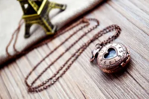 Detailopname van bronzen zakhorloge, opengewerkt hart wijzerplaat en bijpassende ketting.