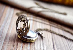 Close-up view of vintage bronze hollow gear pocket watch with long chain on rustic wooden surface.