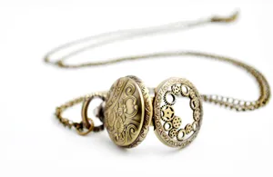 Detail shot of vintage bronze pocket watch with hollow gear cover and long sweater chain necklace.