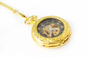 Golden mechanical pocket watch detail view, hollow dial, Roman numerals, watch chain.