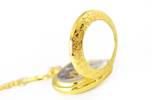 Gold mechanical pocket watch detailed view, vintage carved flip cover with matching chain.