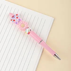Close-up of pink beaded pen with butterfly and daisy silicone charms on a notebook.
