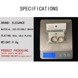 Close-up of zircon wheat hoop earrings on scale showing 9.8g total weight in packaging.