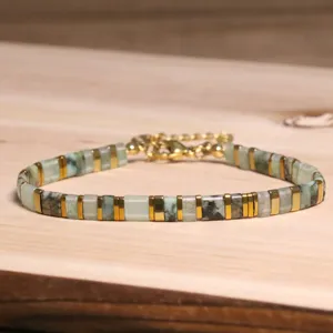 Détail de bracelet en perles Tila avec accents dorés et pierres vertes naturelles