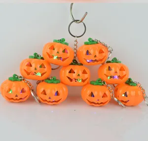 Closeup view of glowing LED Halloween pumpkin keychains featuring orange shells and green stems.