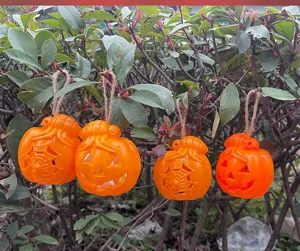 Close-up detail view of orange pumpkin hanging lights displayed on green bushes for Halloween.