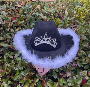 Close-up of black western cowboy hat with rhinestone crown and white feather trim.