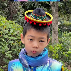 Close-up view of a mini Mexican sombrero headband with colorful woven pattern and red pom-poms.