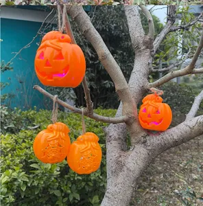 Outdoor hanging Halloween pumpkin lantern scene detail, glowing plastic ornament for party decor.