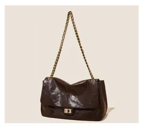 Close up detail of brown leather shoulder bag featuring metallic chain strap and lock.