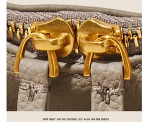 Detailed view of the women's handbag dual gold zippers and pebbled leather pull tabs.