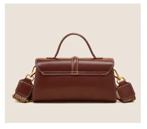 Detailed view of the brown genuine leather top-handle bag featuring wide strap and hardware.